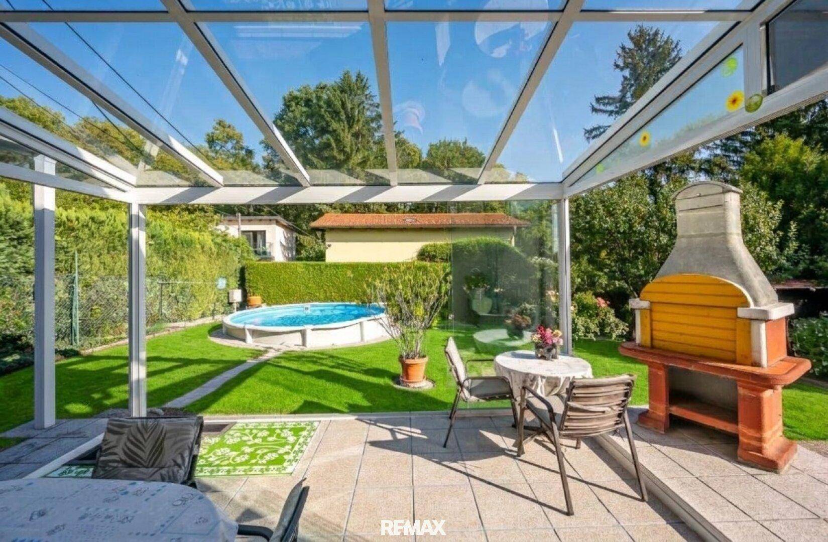 Gemütliche überdachte Terrasse mit Esstisch, Grill und Blick auf den Pool im Garten.