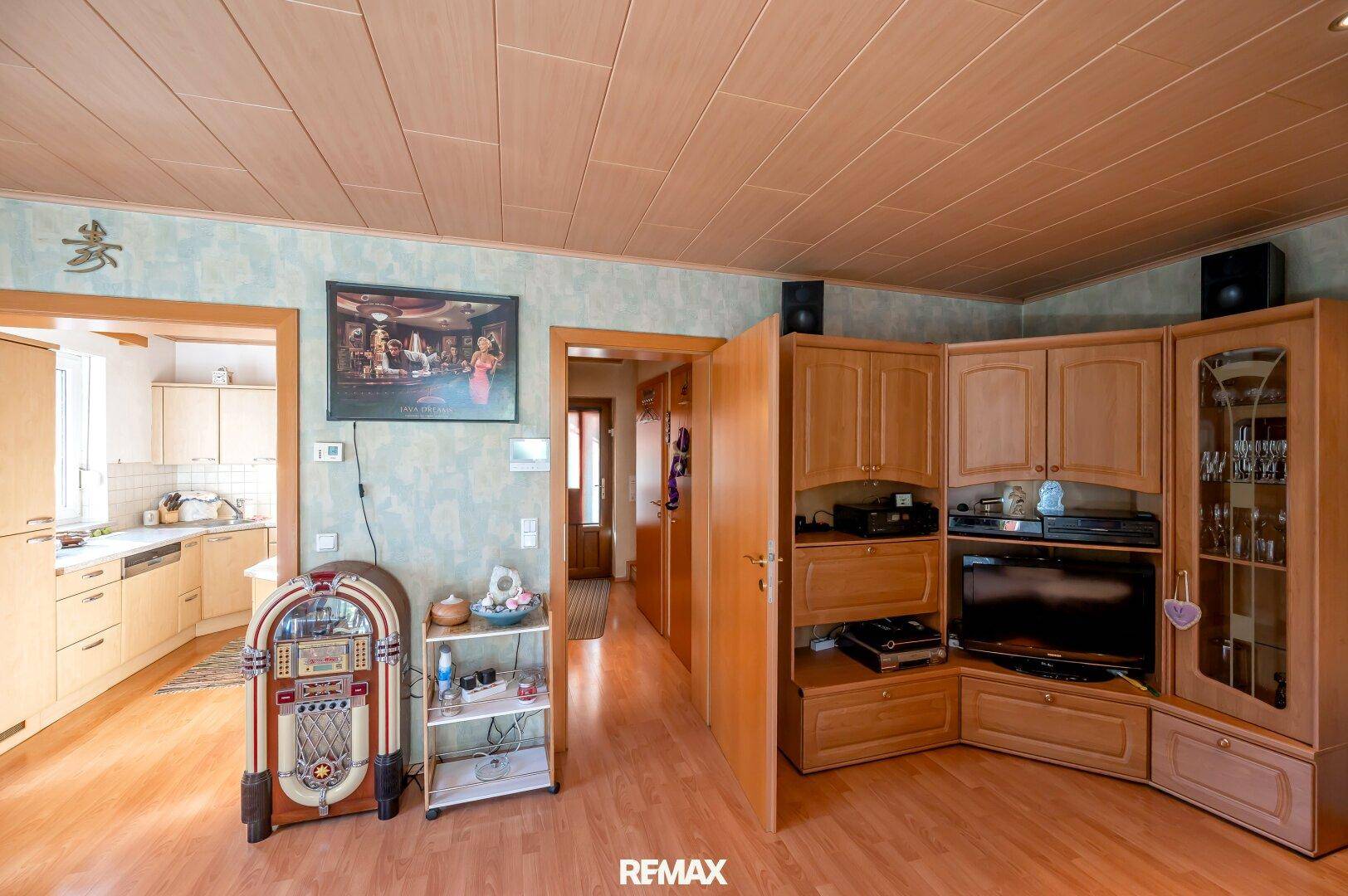 Wohnzimmer mit Holzboden, Unterhaltungsmöbeln und Blick in die angrenzende Küche.