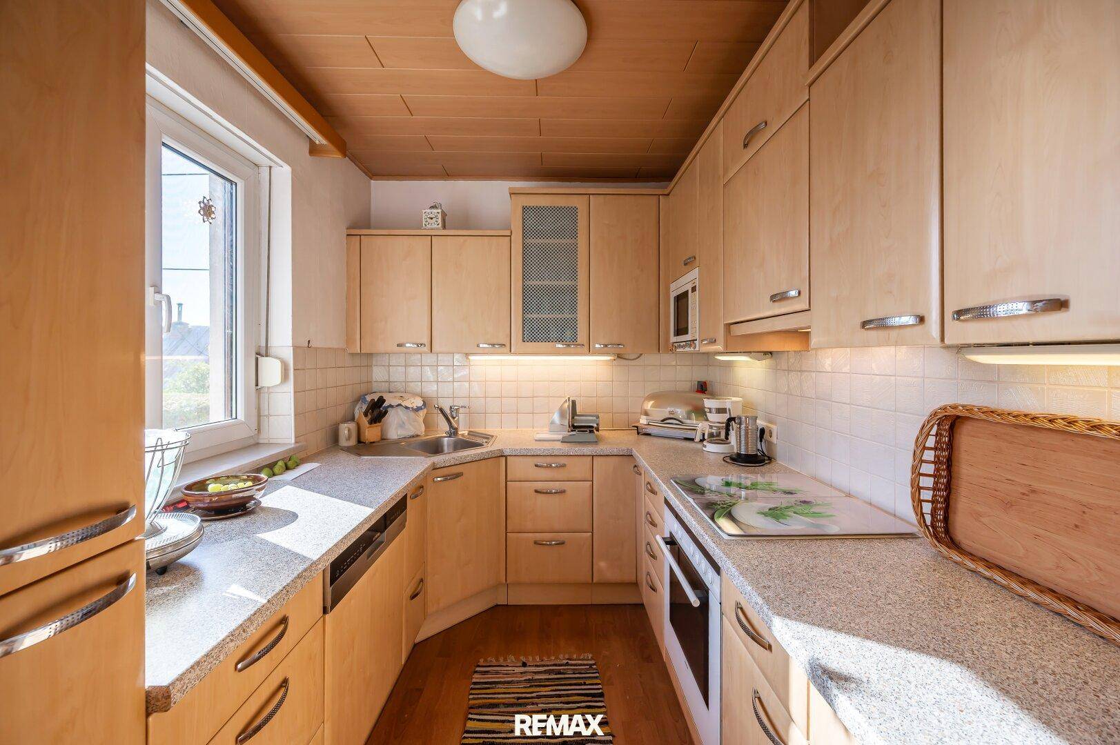 Funktionale Küche mit hellen Holzschränken, Fliesenrückwand und Fenster.