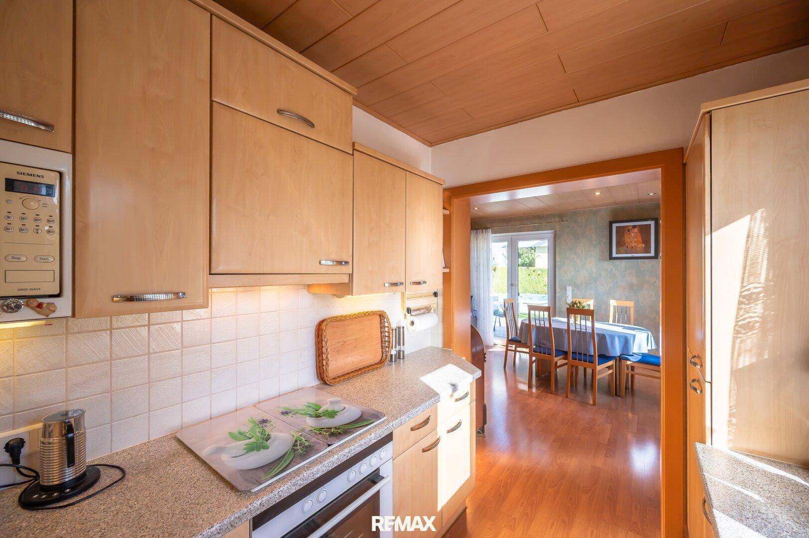 Helle Küche mit Holzfronten und offenem Durchgang zum Essbereich des Hauses.