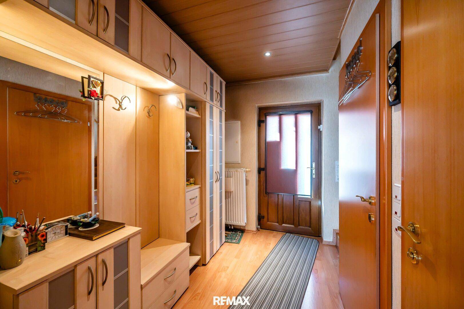 Eingangsbereich mit Einbauschränken, Holzboden und Garderobe für Besucher.