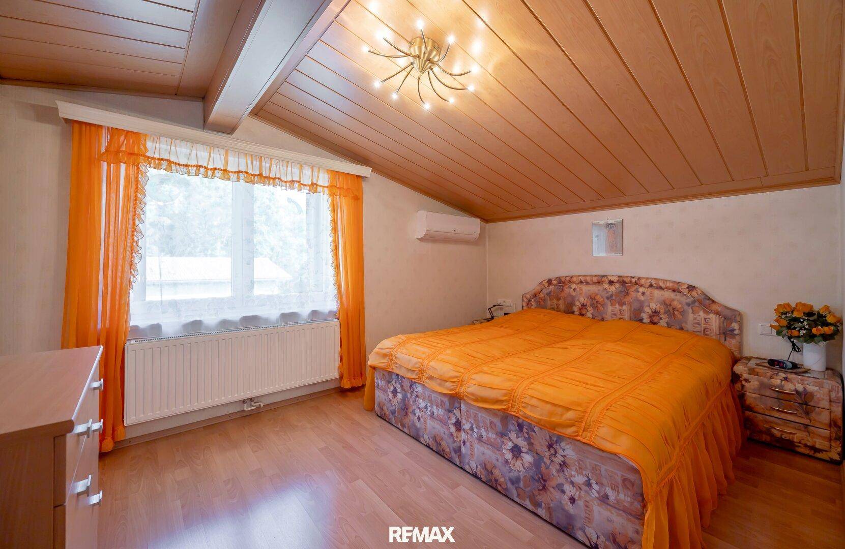 Gemütliches Schlafzimmer mit Holzboden, Dachschräge und Klimaanlage.