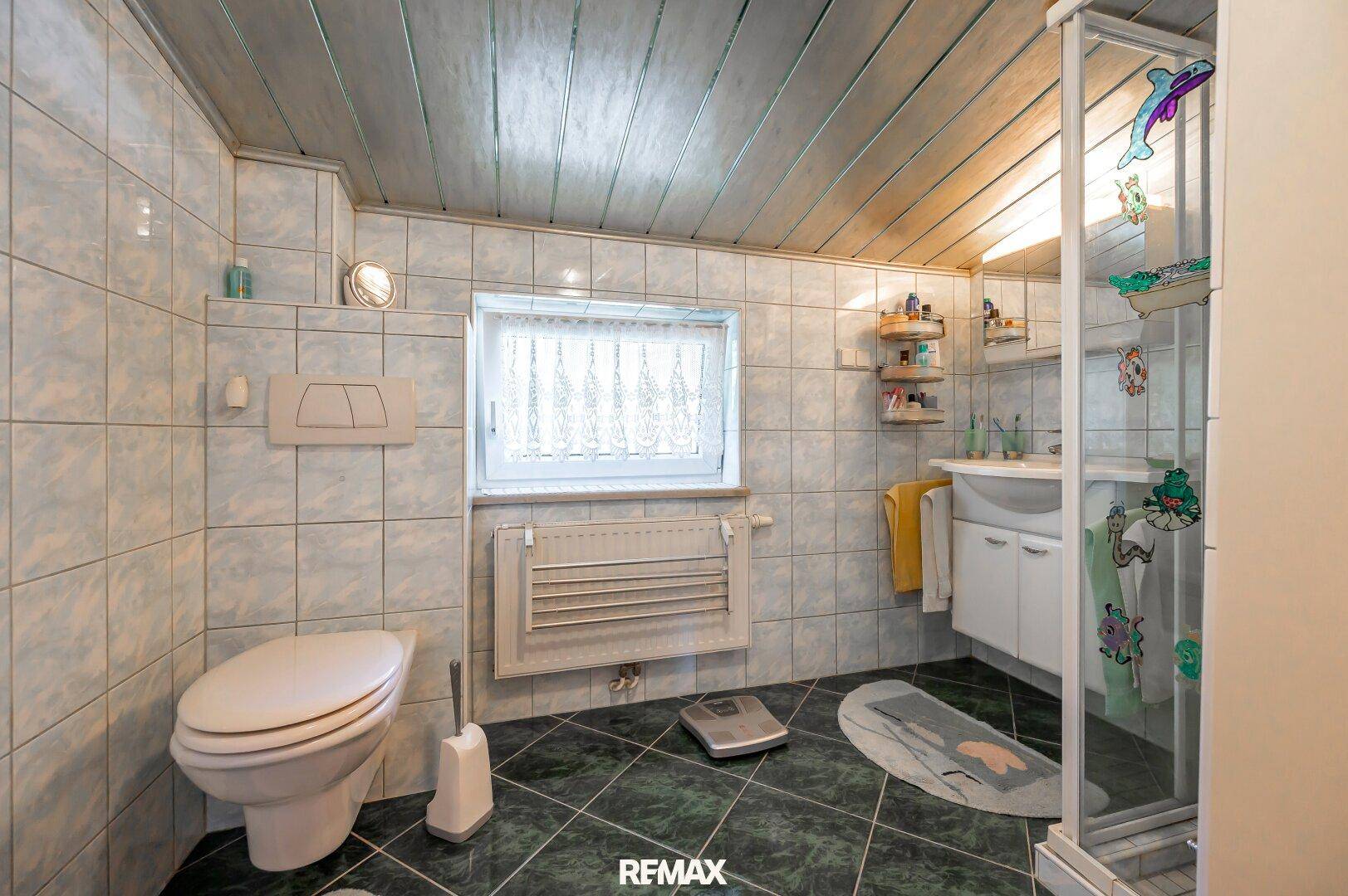 Badezimmer mit hellblauen Fliesen, Dusche und Fenster für Tageslicht.