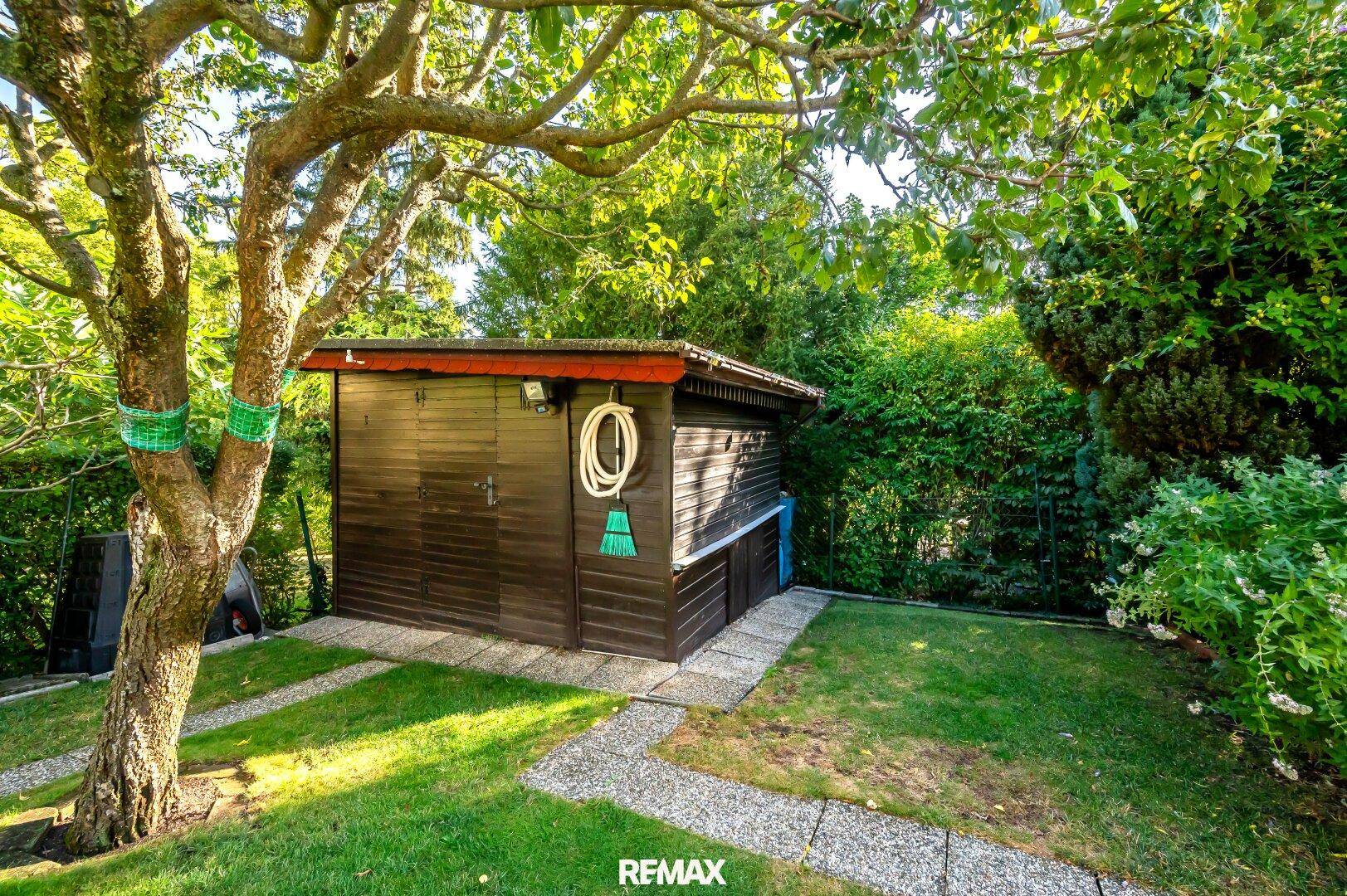 Praktischer Gartenschuppen aus Holz, umgeben von Bäumen und Grünflächen.