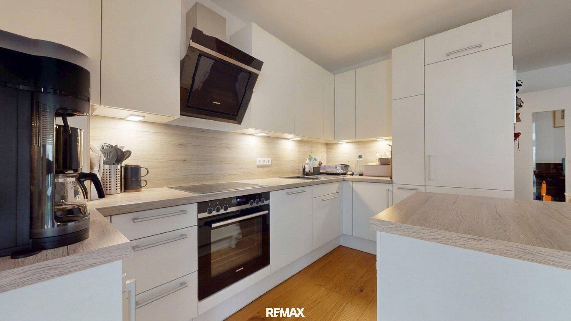 Moderne Einbauküche mit weißen Fronten, Holz-Arbeitsplatten und integrierten Geräten.