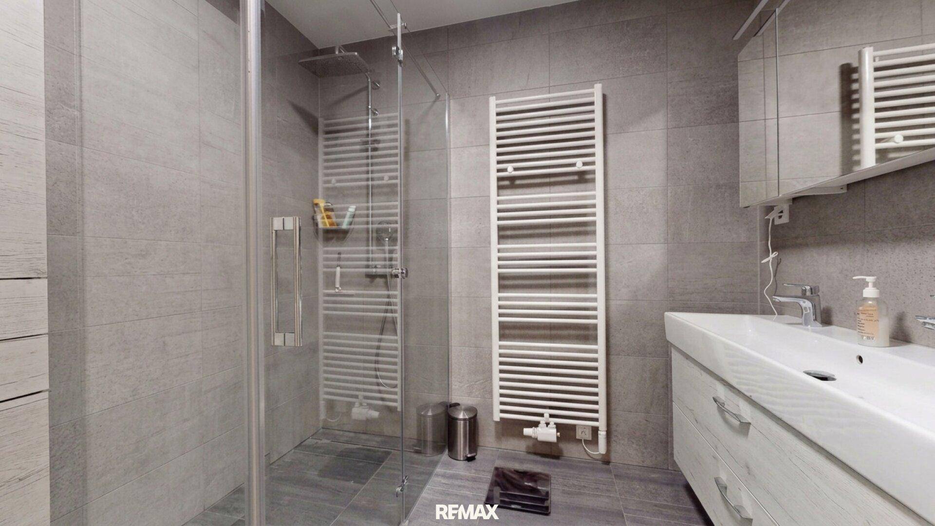 Modernes Badezimmer mit begehbarer Dusche, grauen Fliesen und praktischem Handtuchheizkörper.