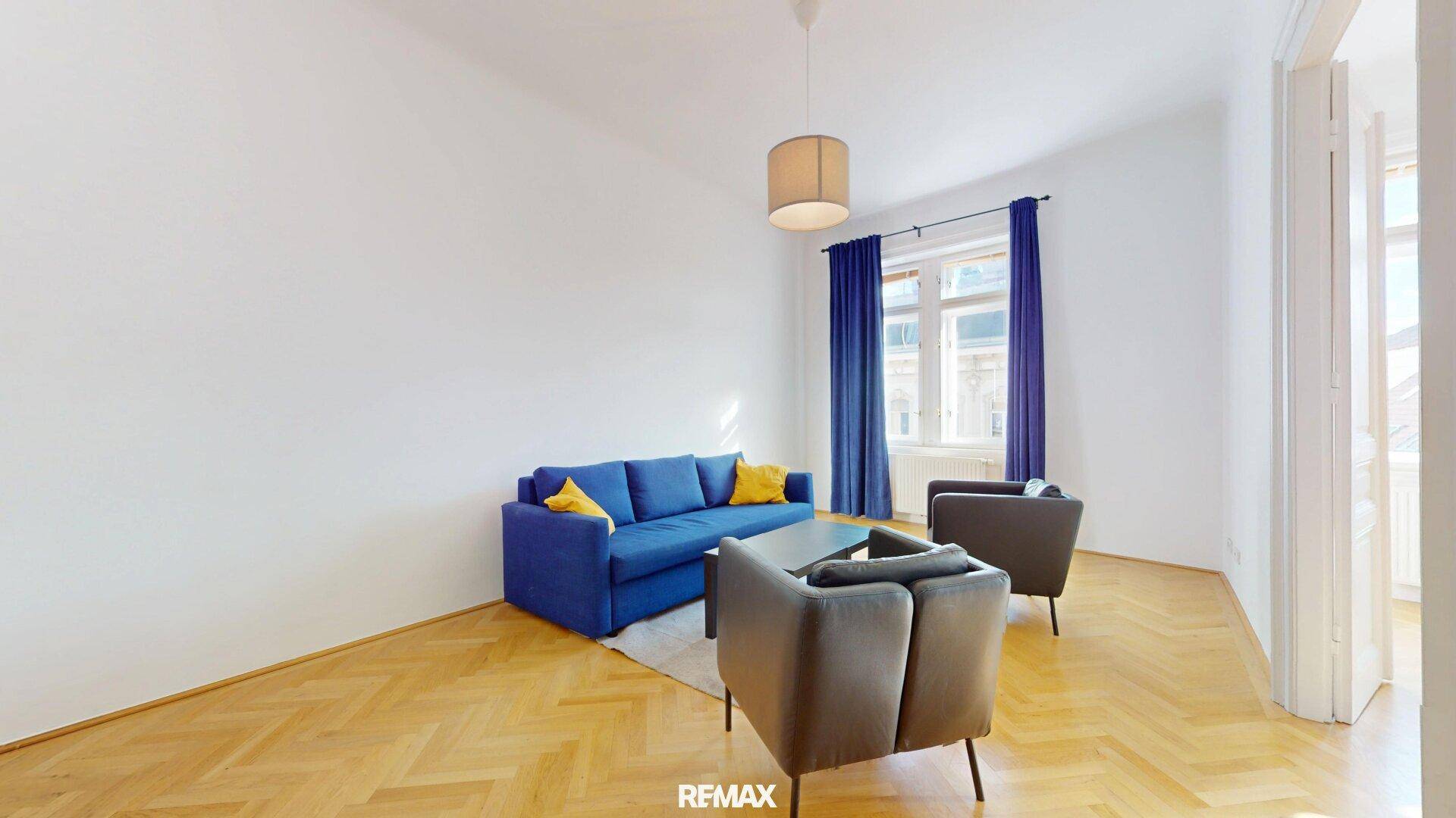 Gemütliches Wohnzimmer mit blauem Sofa, dunklen Sesseln und Parkettboden.