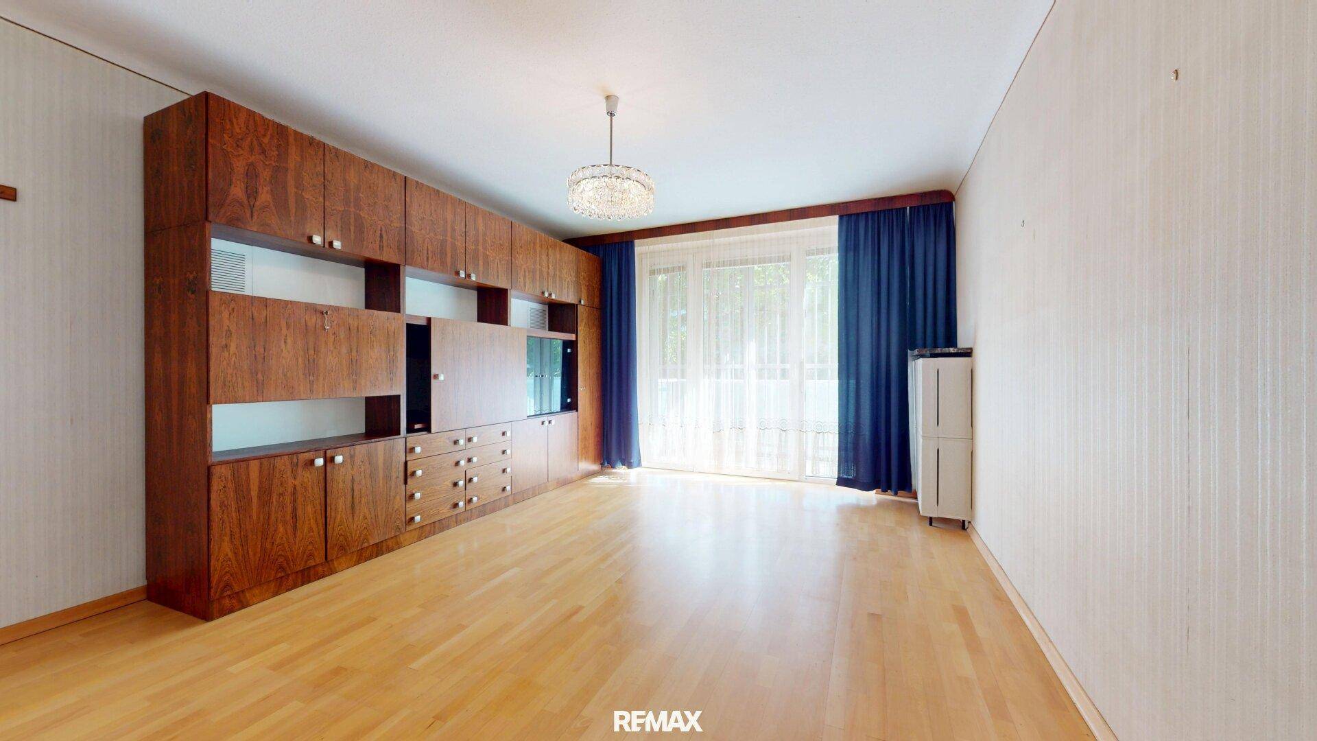 Geräumiges Wohnzimmer mit Holzeinbauschrank und Zugang zum Balkon.