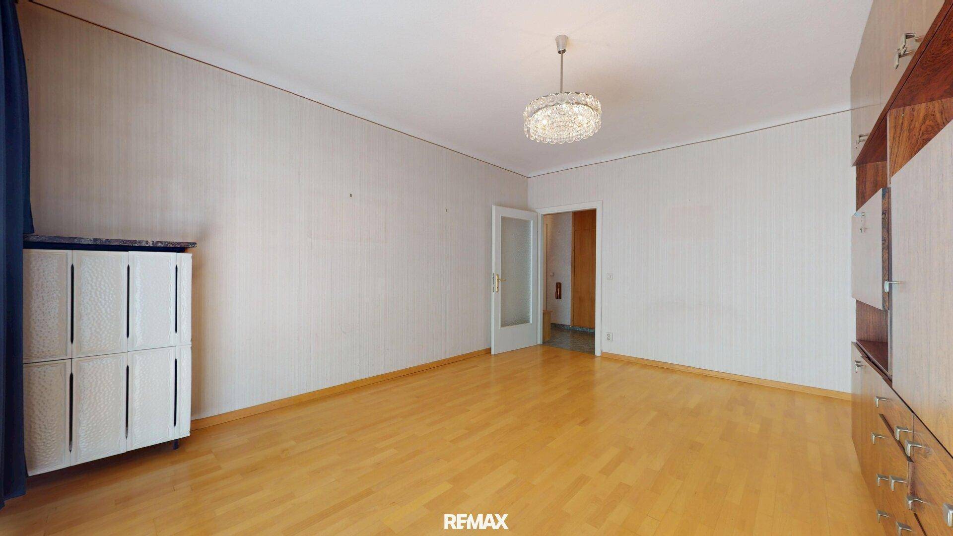 Helles Wohnzimmer mit Parkettboden und Zugang zu weiteren Räumen.