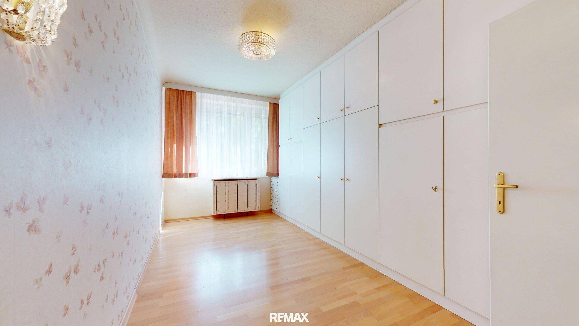 Schlafzimmer mit Einbauschränken, Parkettboden und Fenster.