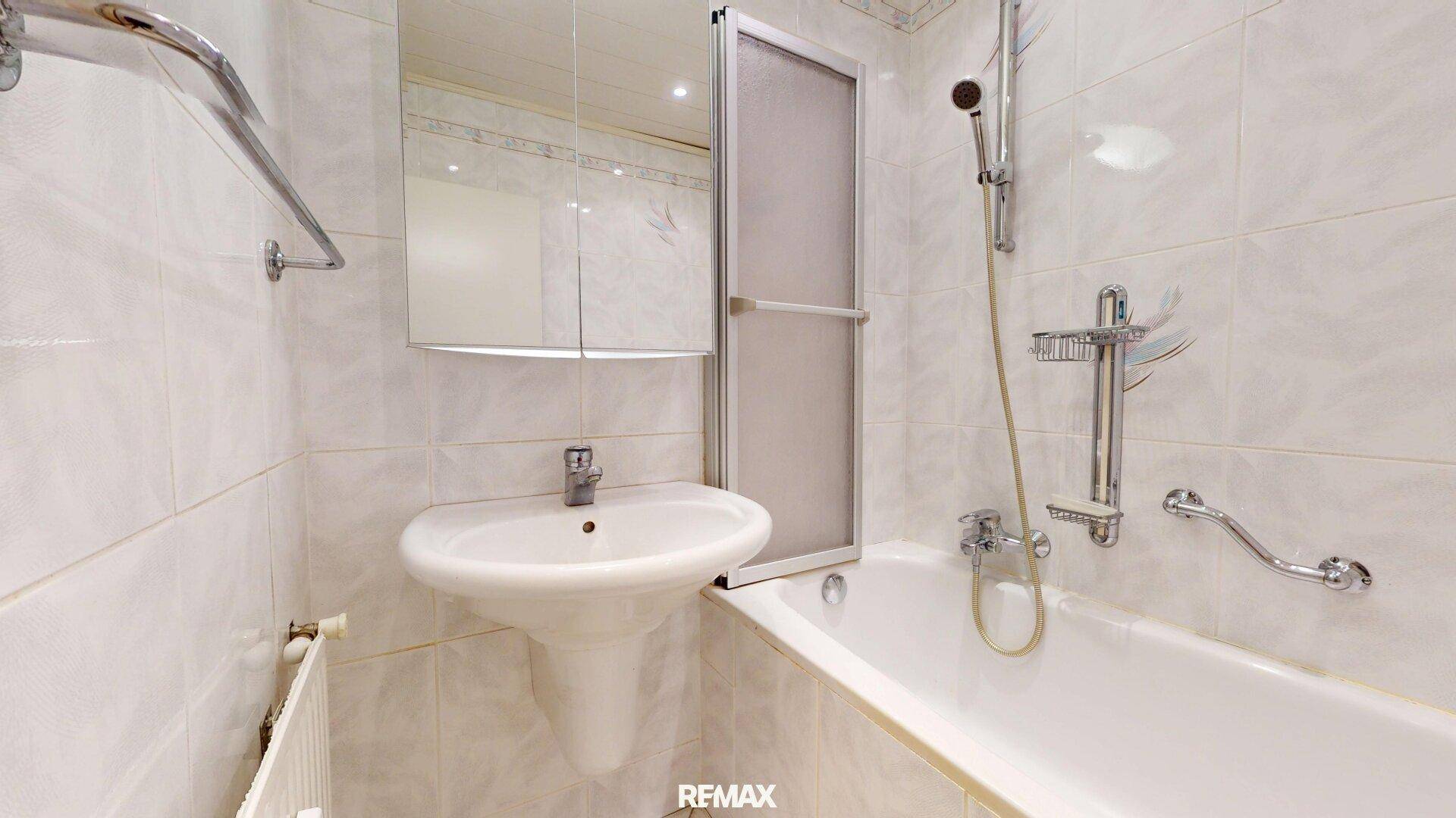 Badezimmer mit Badewanne, Waschbecken und weißen Fliesen.