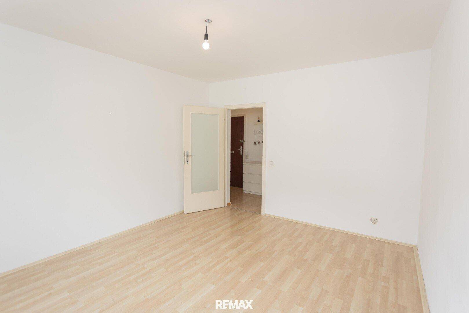 Leeres Zimmer mit Laminatboden und einer Tür, die zu einem weiteren Raum führt.
