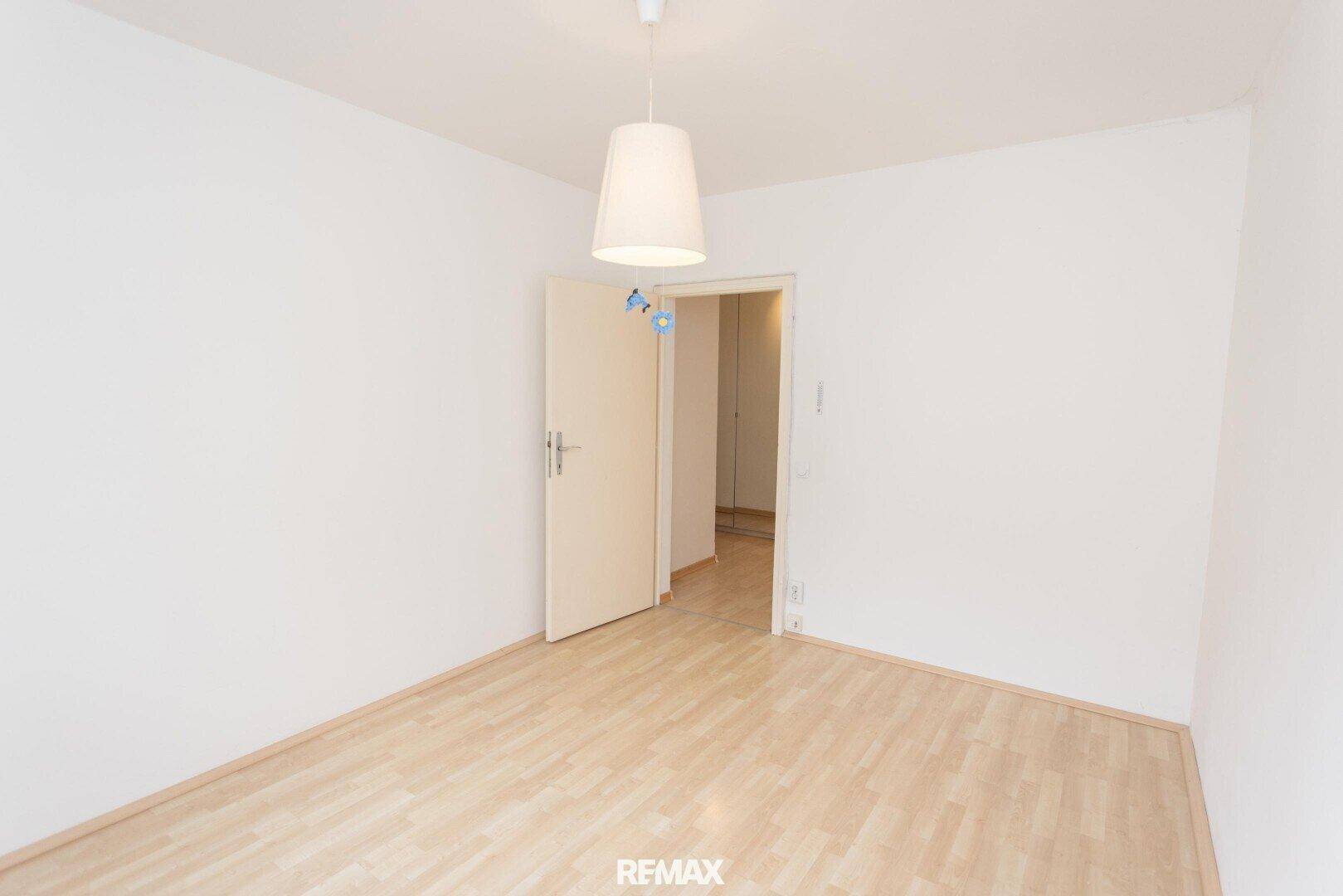 Leeres Schlafzimmer mit Laminatboden und einer offenen Tür zu einem angrenzenden Bereich.