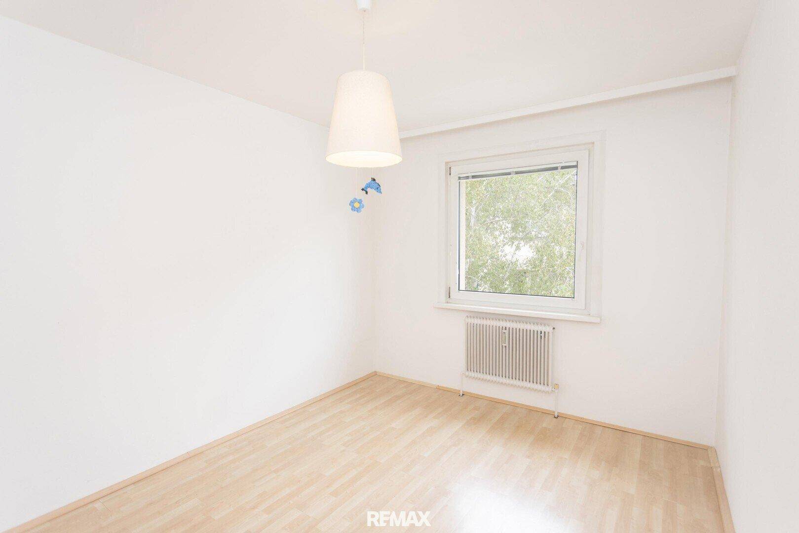 Helles Schlafzimmer mit Laminatboden, Fenster und einer einfachen Deckenleuchte.