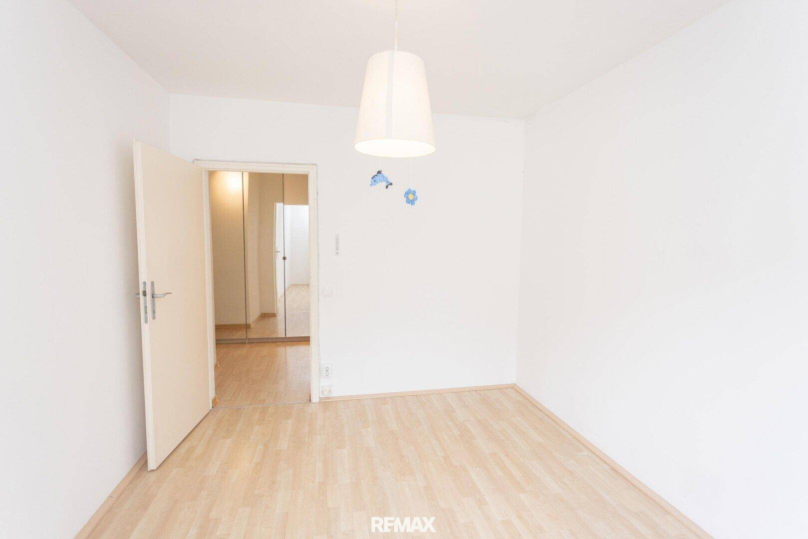 Schlafzimmer mit Laminatboden und einer Tür, die zu einem Bereich mit Spiegelschränken führt.