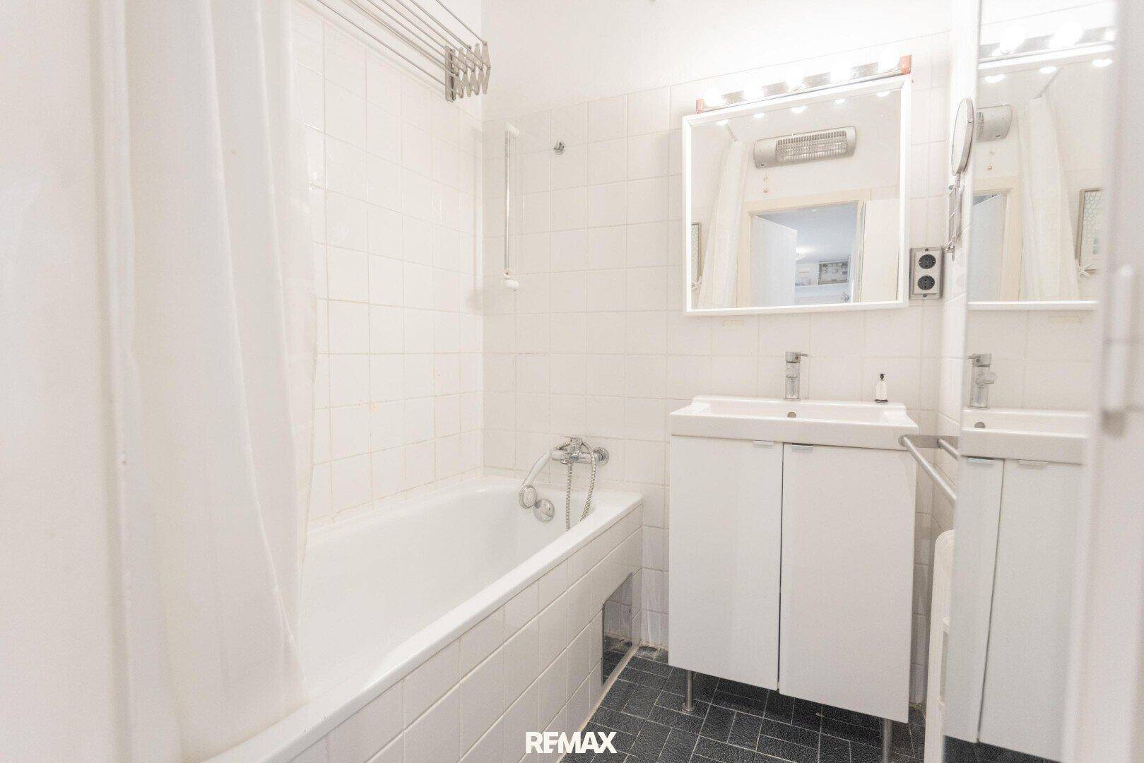 Funktionales Badezimmer mit Badewanne und Waschbecken, ausgestattet mit weißen Fliesen.