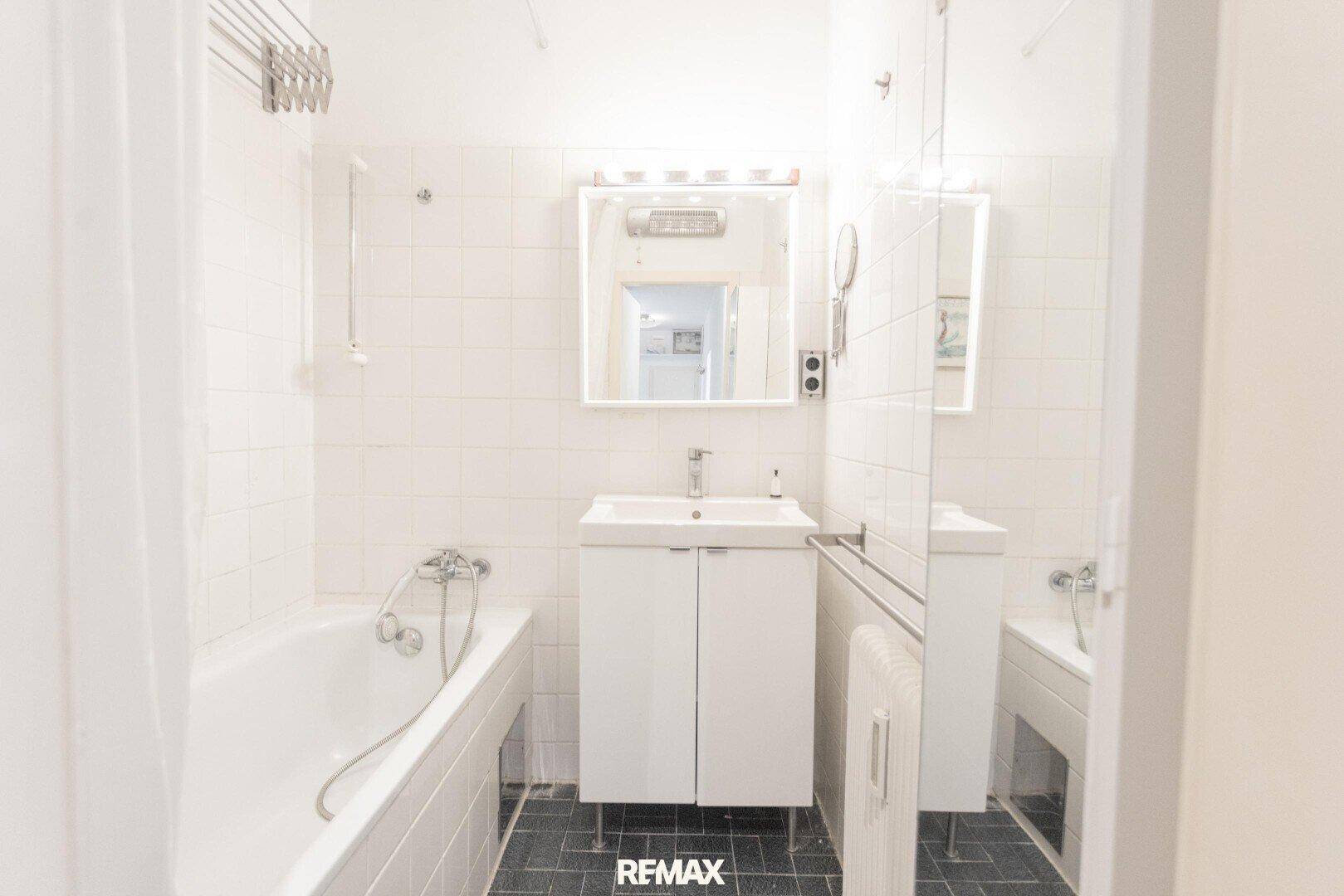 Helles Badezimmer mit Badewanne, Waschbecken und Spiegelschrank, weiß gefliest.