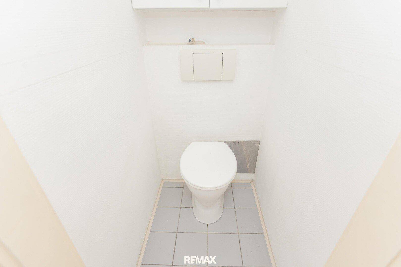 Separate Toilette mit wandmontiertem WC und hellgrauen Bodenfliesen.