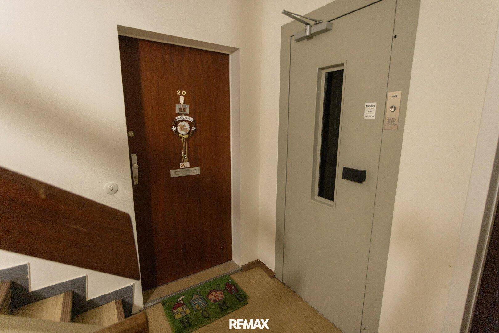 Eingangstür einer Wohnung neben einem Aufzug im Treppenhaus.