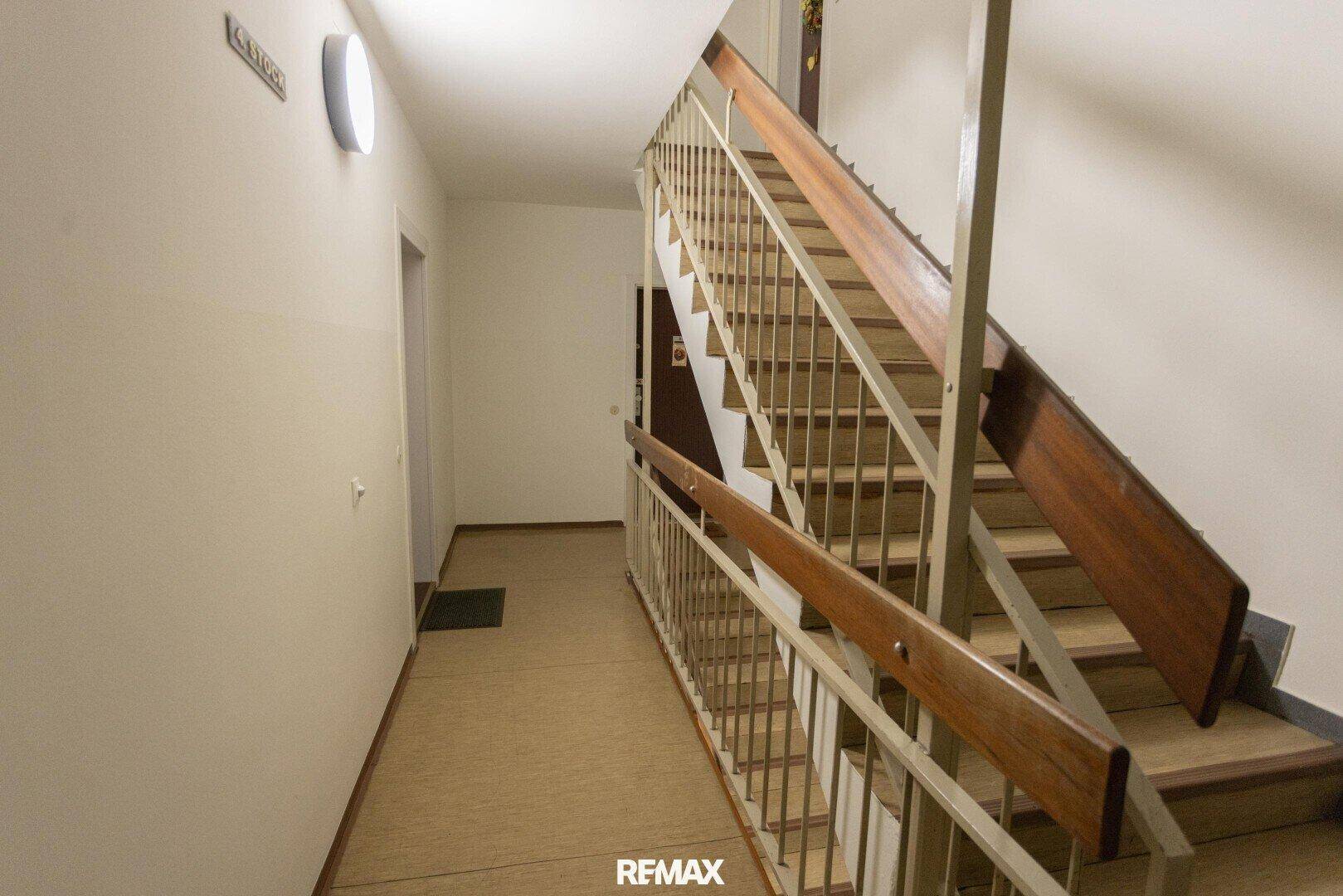 Treppenhaus mit Holzgeländer und Teppichboden, das zu den oberen Stockwerken führt.