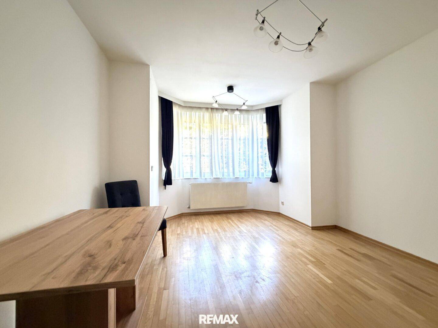 Geräumiges Zimmer mit Parkettboden und einem großen Erkerfenster, das den Raum erhellt.