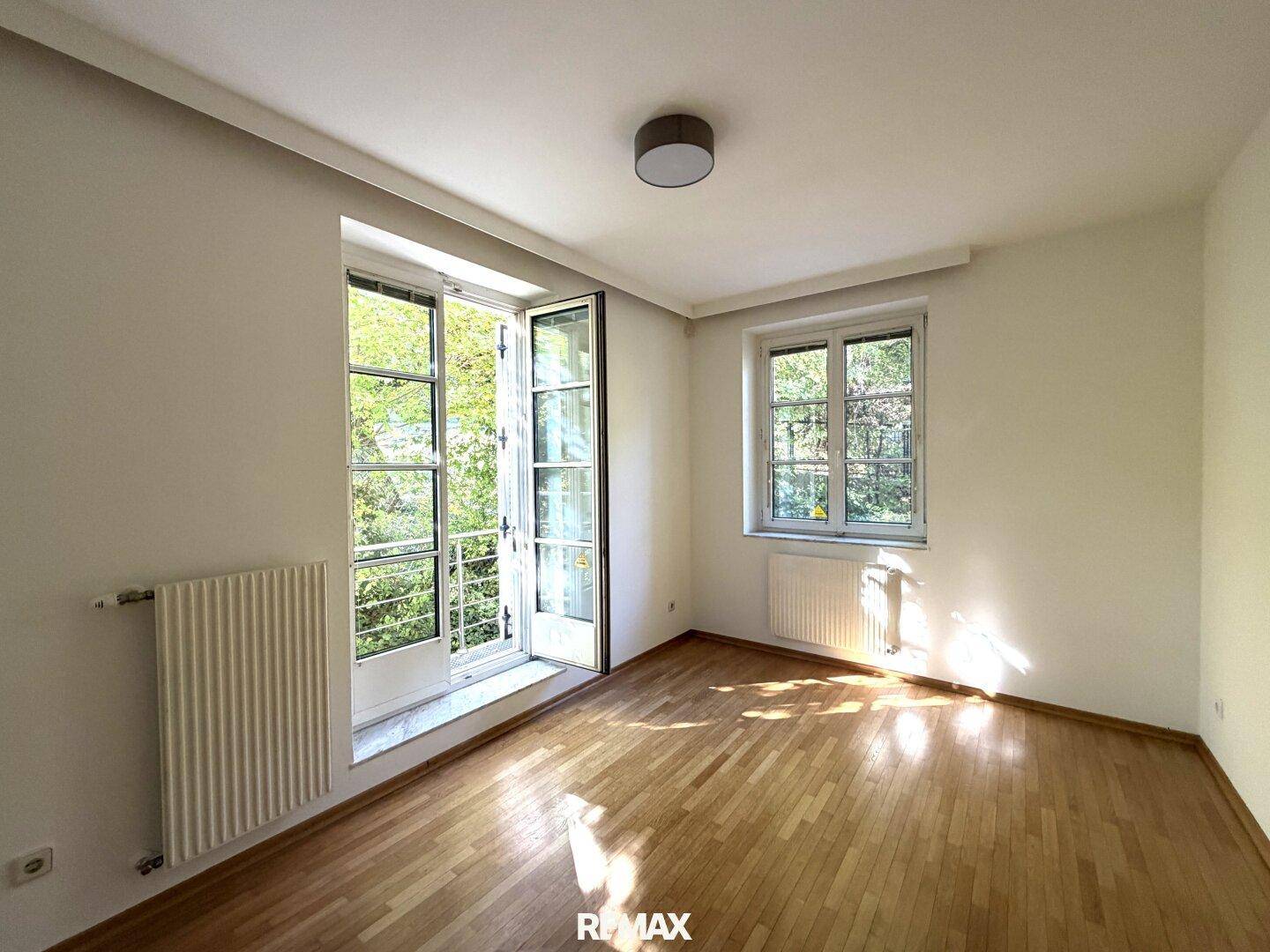 Lichtdurchfluteter Raum mit Holzboden und Fenstern, die einen schönen Blick auf die Bäume bieten.