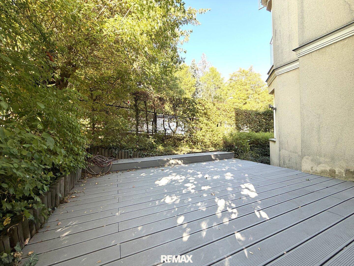 Eine geräumige Holzterrasse umgeben von üppigem Grün und Bäumen, ideal zum Entspannen.