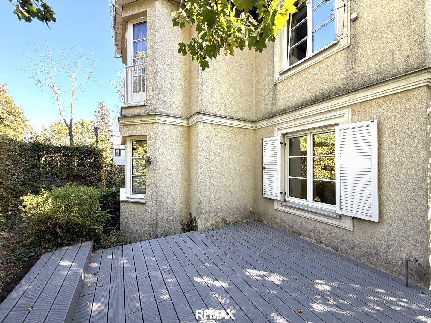 Außenansicht des Gebäudes mit einer Holzterrasse und Fenstern mit weißen Fensterläden.
