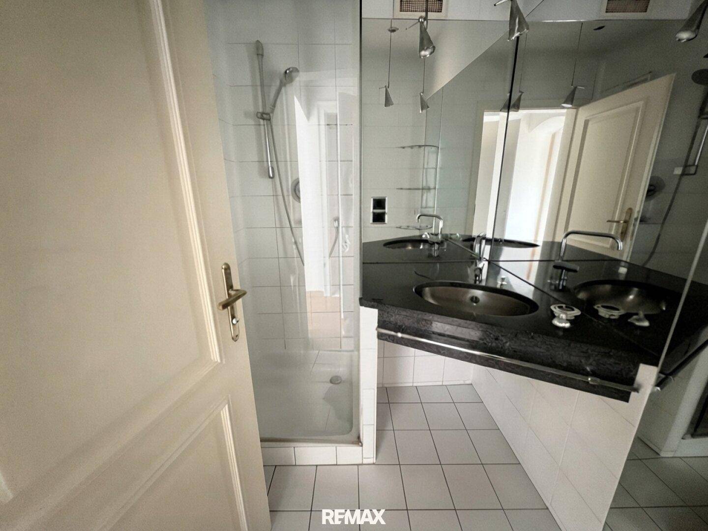 Modernes Badezimmer mit Doppelwaschbecken, großer Spiegelfläche und einer Duschkabine.