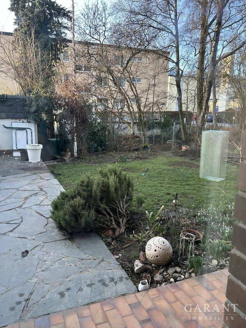 Grüner Gartenbereich mit Rasenfläche und Sträuchern, gesehen durch ein Fenster.