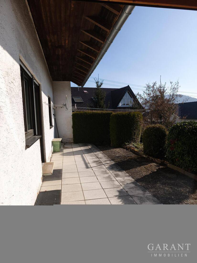 Seitliche Terrasse mit Fliesenboden und Blick auf die Nachbarschaft unter klarem Himmel.