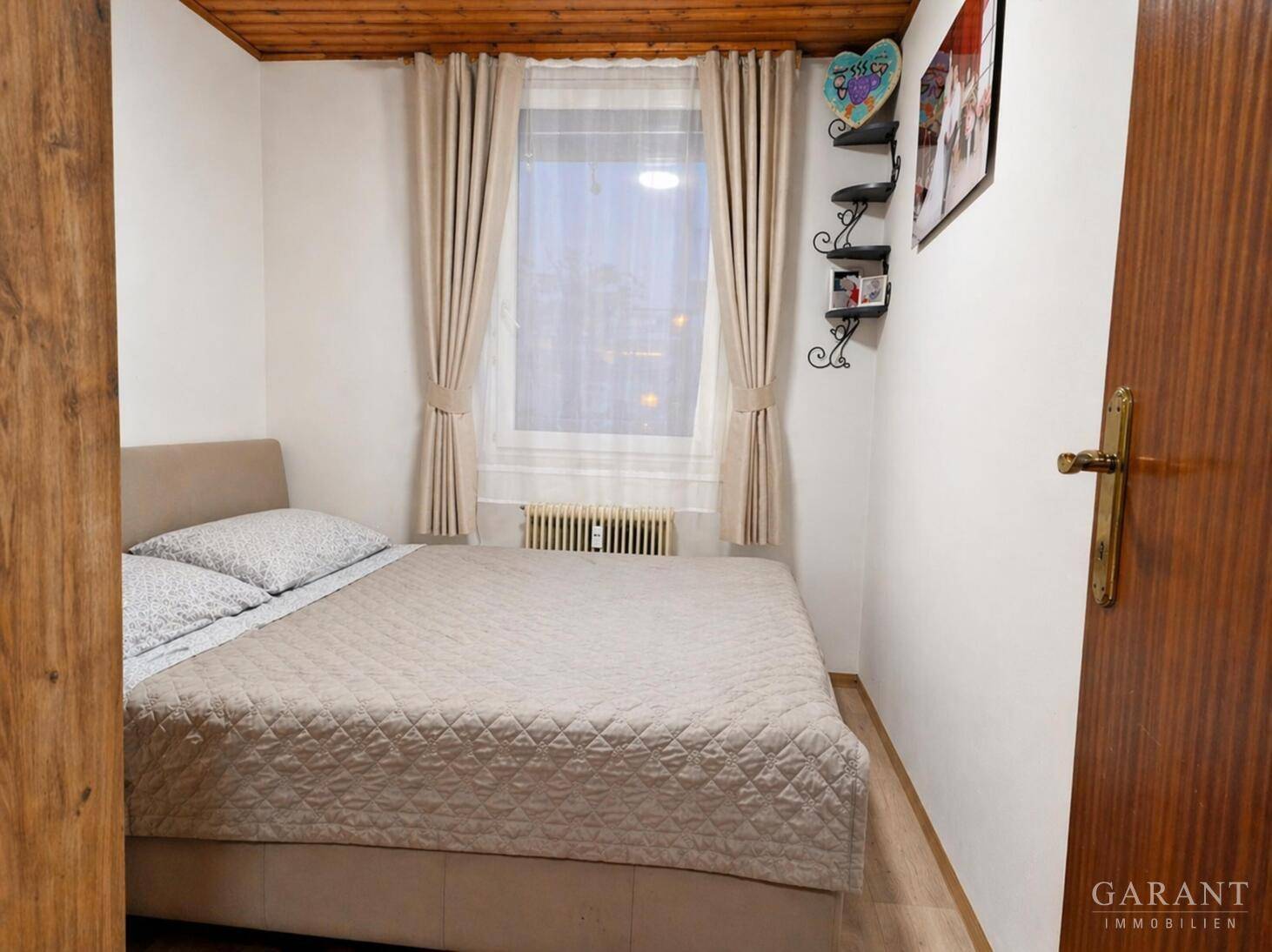 Gemütliches Schlafzimmer mit Doppelbett, Laminatboden und Fenster mit Vorhängen.