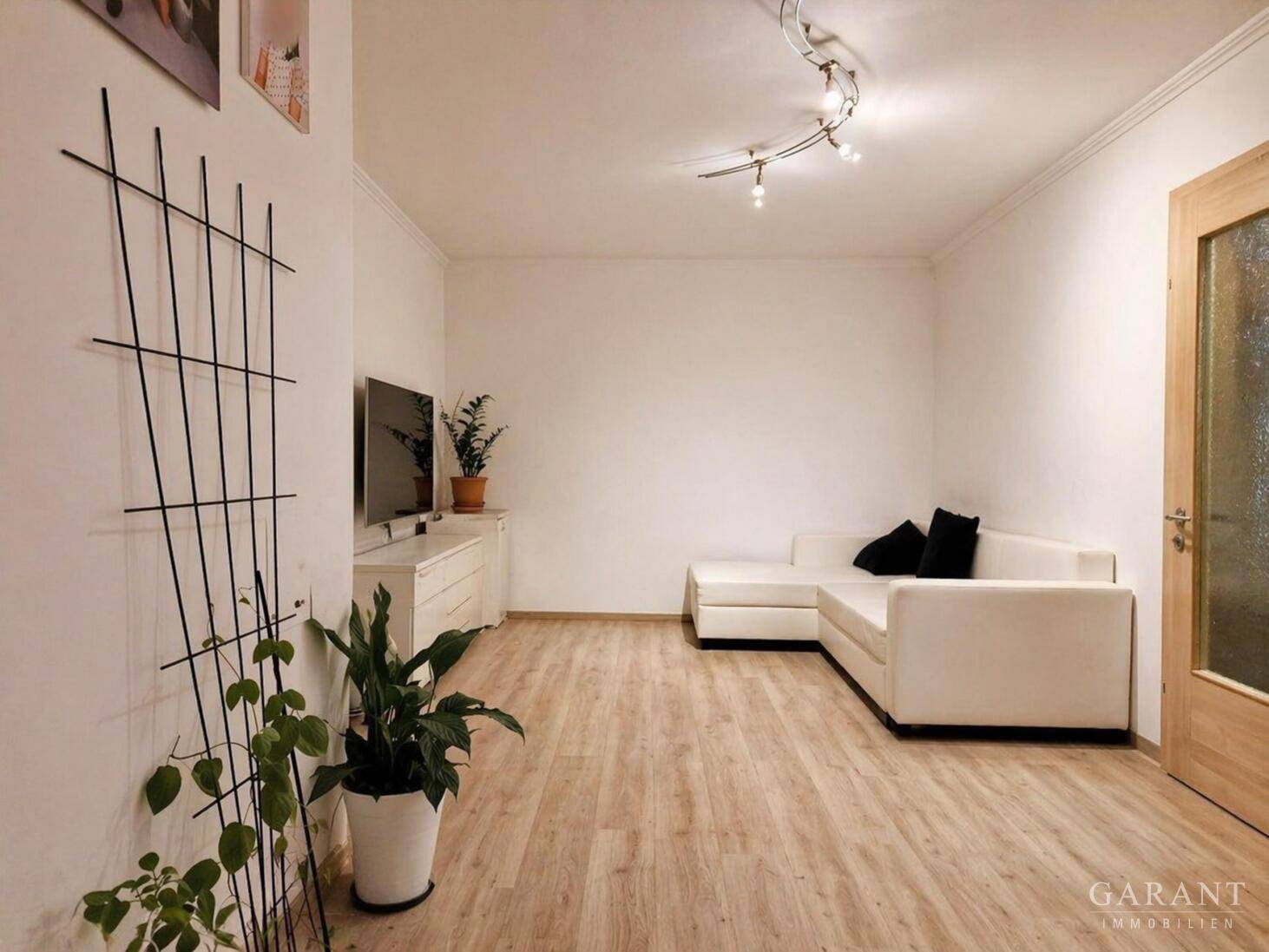 Helles Wohnzimmer mit weißem Sofa, Laminatboden und moderner Deckenbeleuchtung.