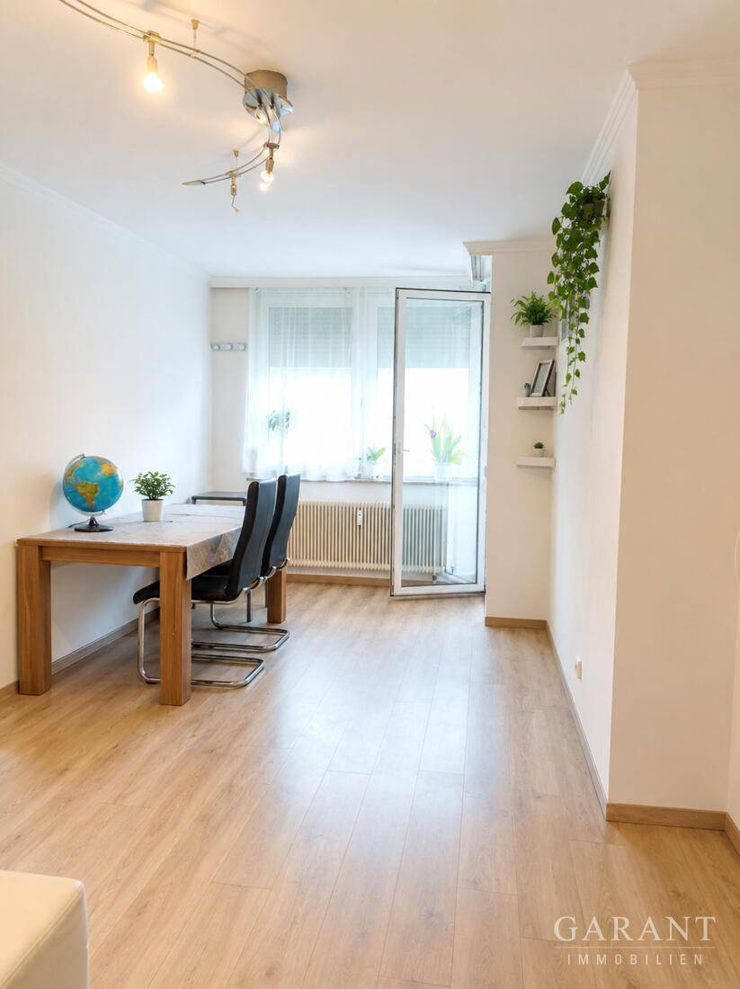 Heller Wohn- und Essbereich mit Laminatboden, Esstisch und Zugang zum Balkon.
