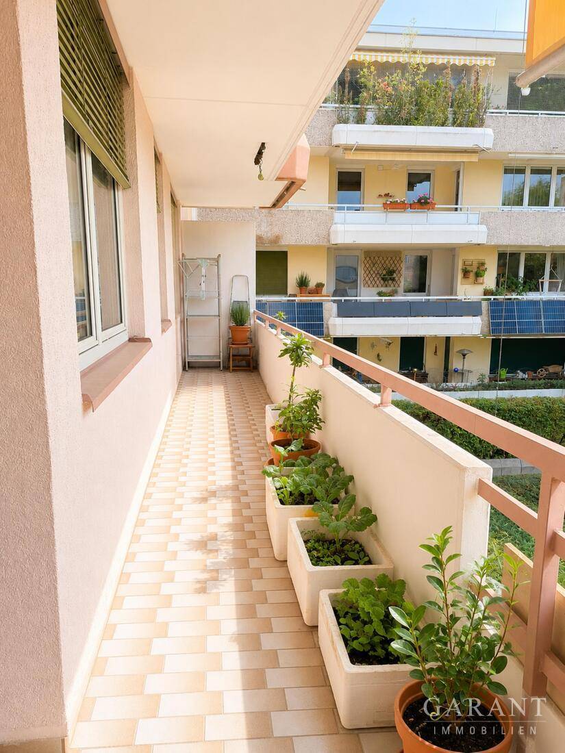Langer, schmaler Balkon mit Fliesenboden und Pflanzen in Töpfen, mit Blick auf andere Gebäude.
