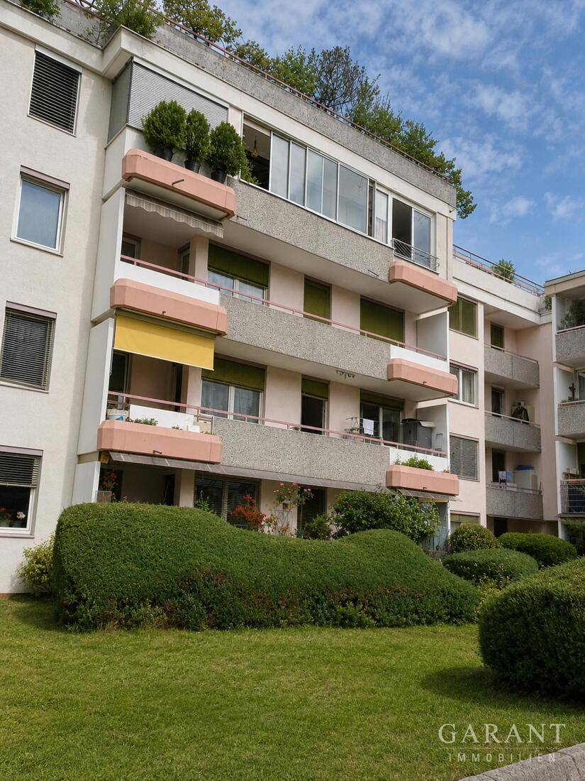 Mehrstöckiges Wohngebäude mit Balkonen und begrüntem Dach, umgeben von Rasenflächen.