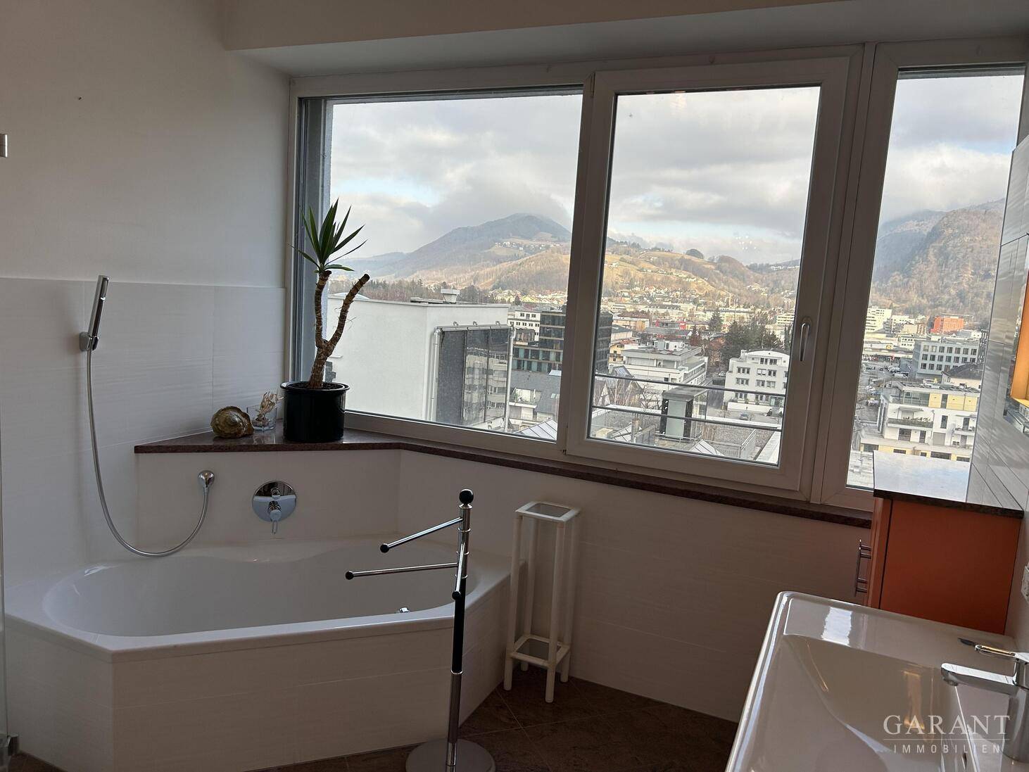 Helles Badezimmer mit Eckbadewanne und großem Fenster mit Blick auf die Stadt und Berge.