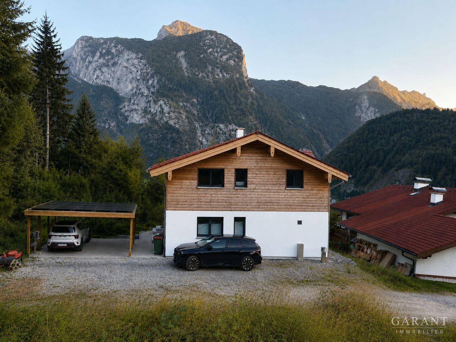 Modernes Einfamilienhaus mit Holzfassade, Carport und Bergblick in ländlicher Umgebung.