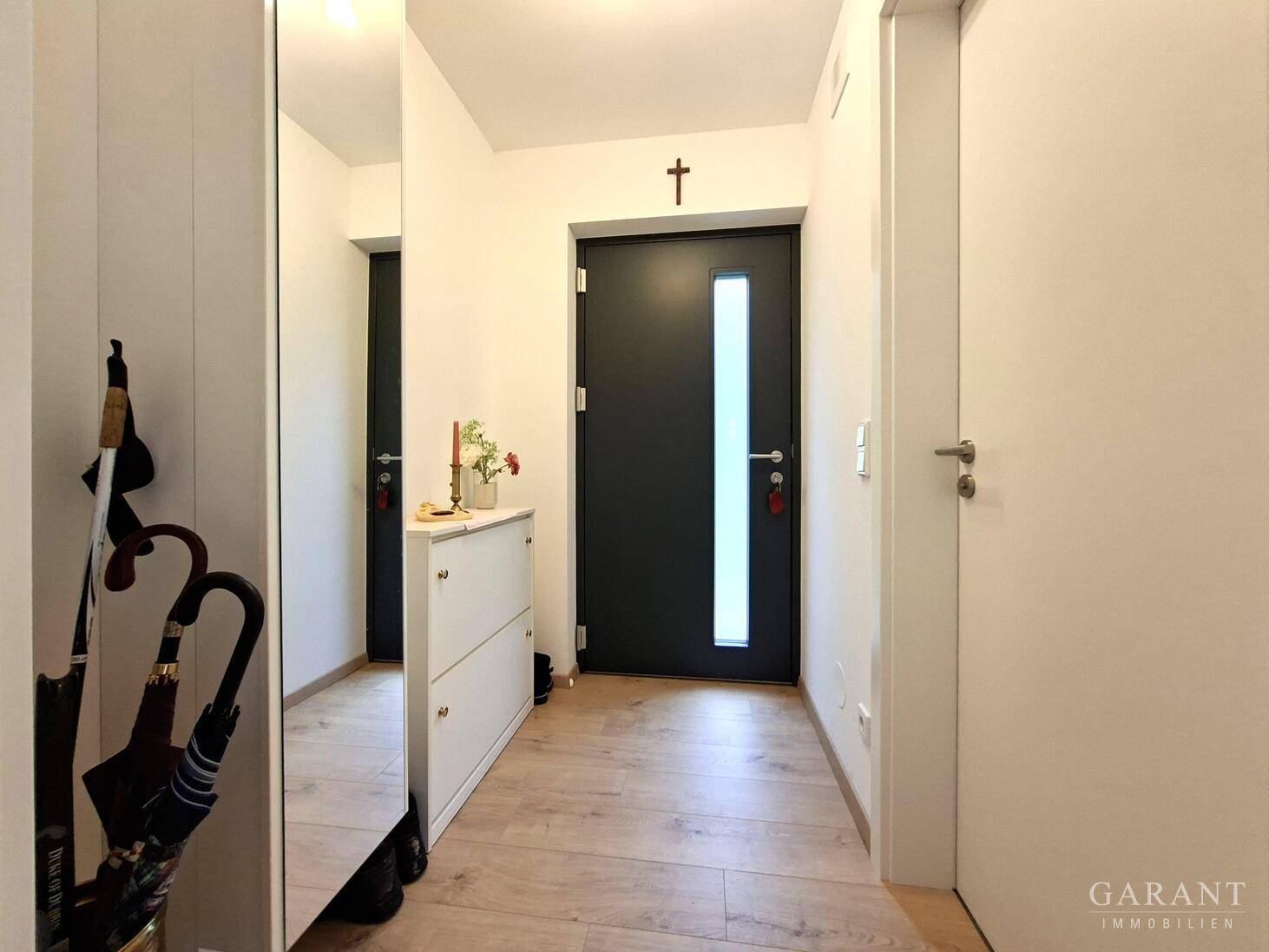 Heller Eingangsbereich mit Garderobe, Spiegel und moderner Eingangstür.