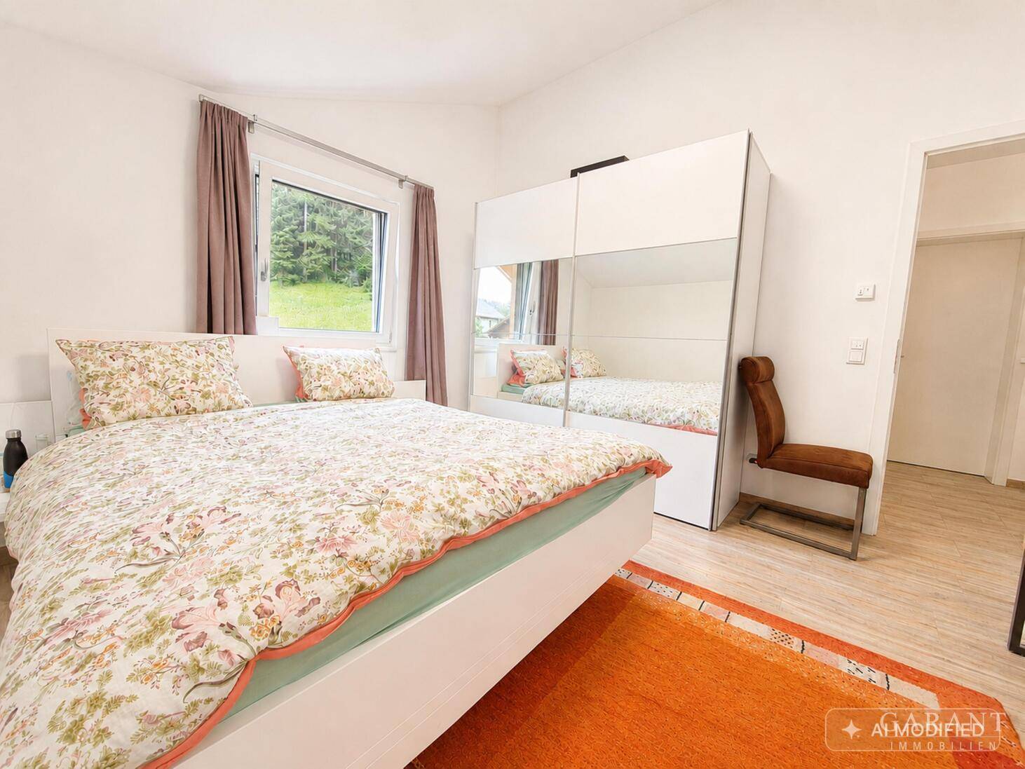 Helles Schlafzimmer mit Doppelbett, Spiegelschrank und Fenster mit Blick ins Grüne.