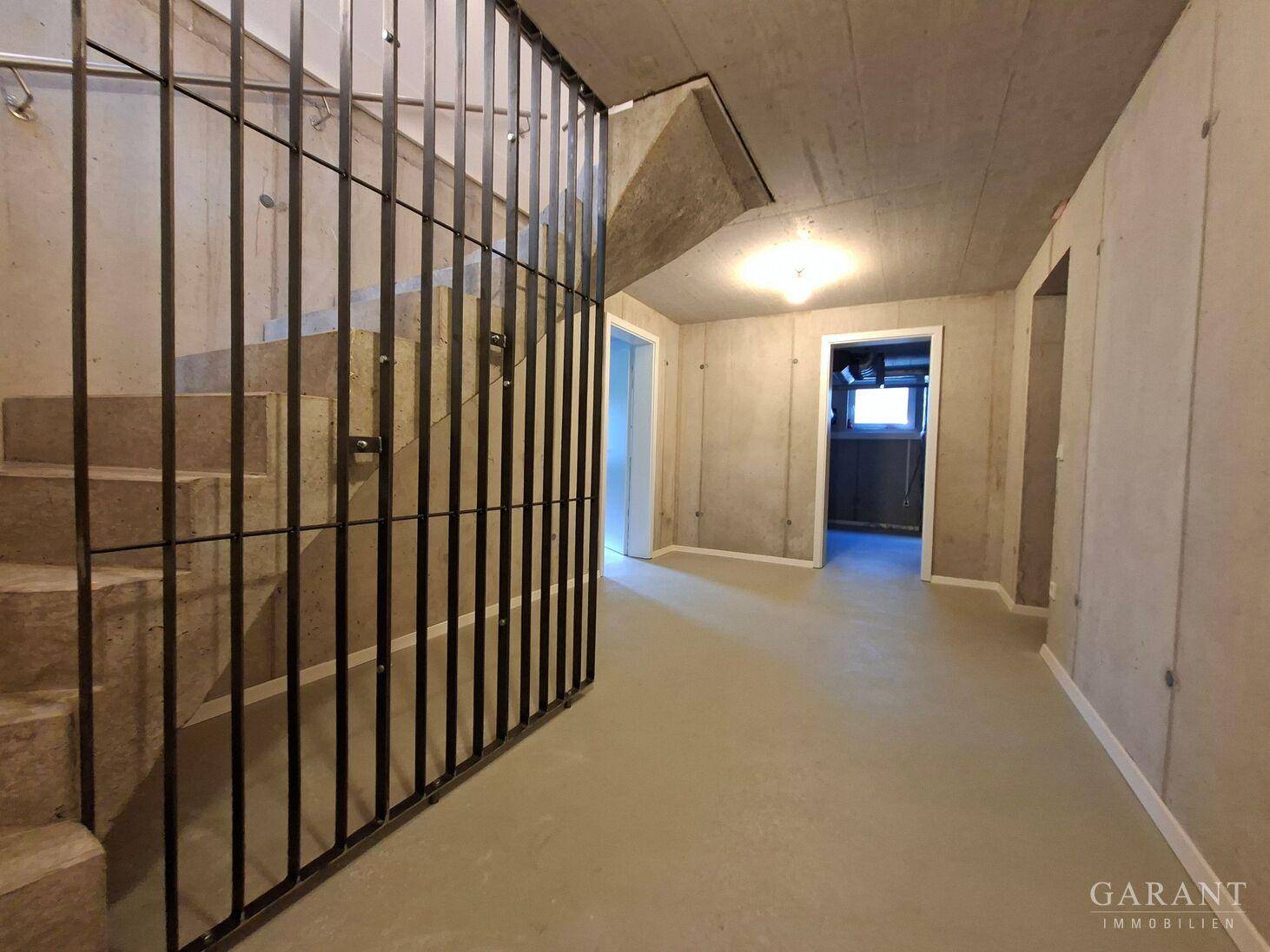 Kellerflur mit Betontreppe und Metallgitter, führt zu weiteren Kellerräumen.