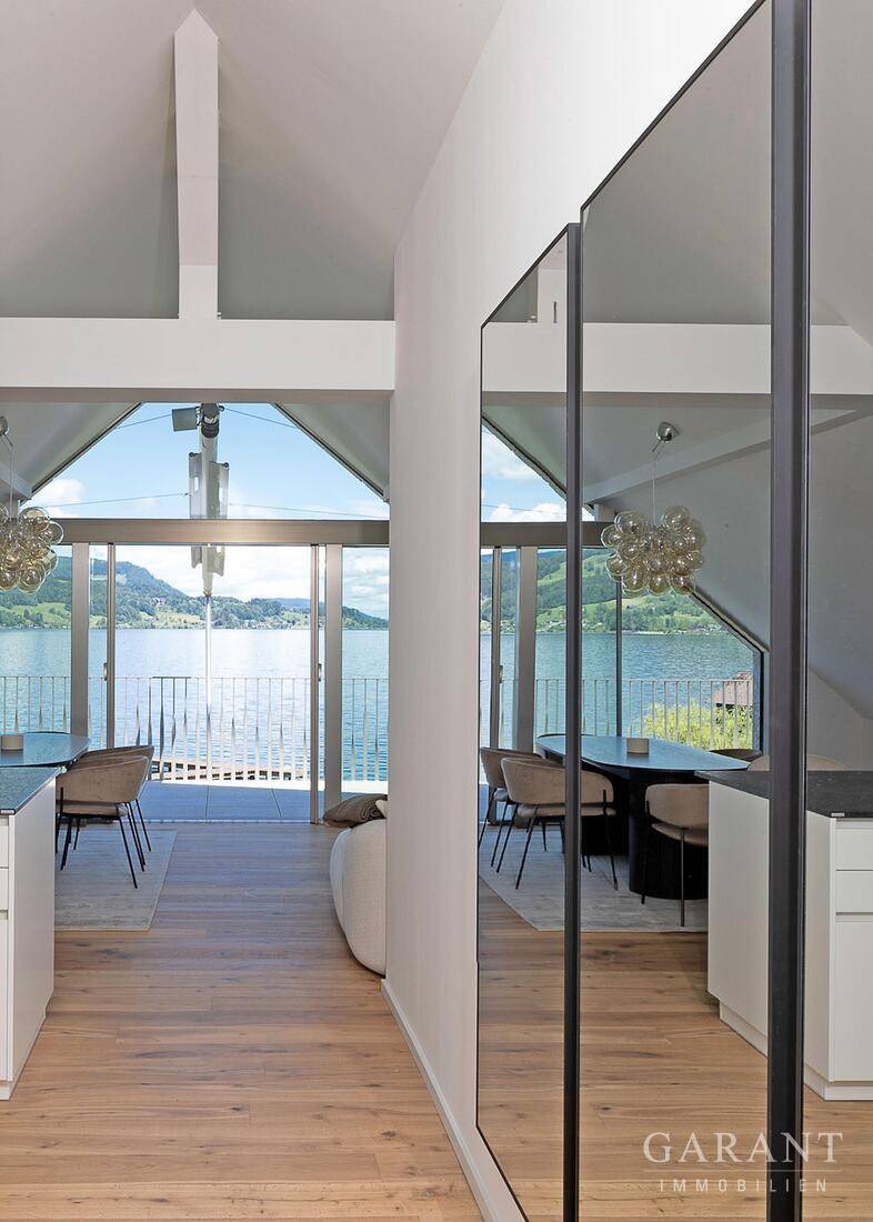 Heller Wohn- und Essbereich mit Seeblick, hohen Decken und modernen Spiegeln, die den Raum erweitern.