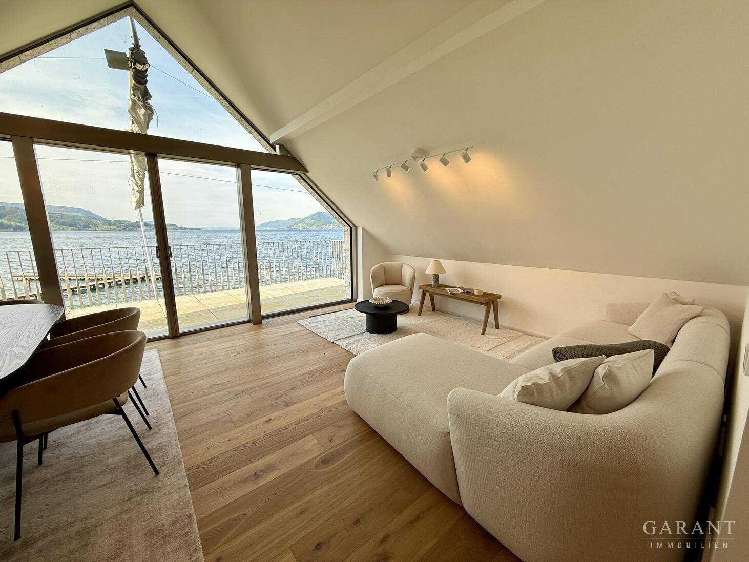 Gemütliches Wohnzimmer mit Seeblick, modernen Möbeln und schrägen Dachfenstern, die viel Licht hereinlassen.