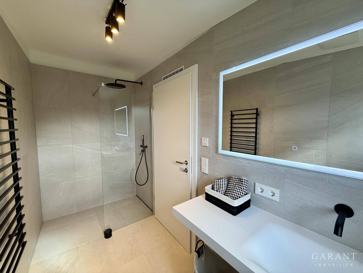 Modernes Badezimmer mit ebenerdiger Dusche, eleganten Fliesen und beheiztem Handtuchhalter für Komfort.