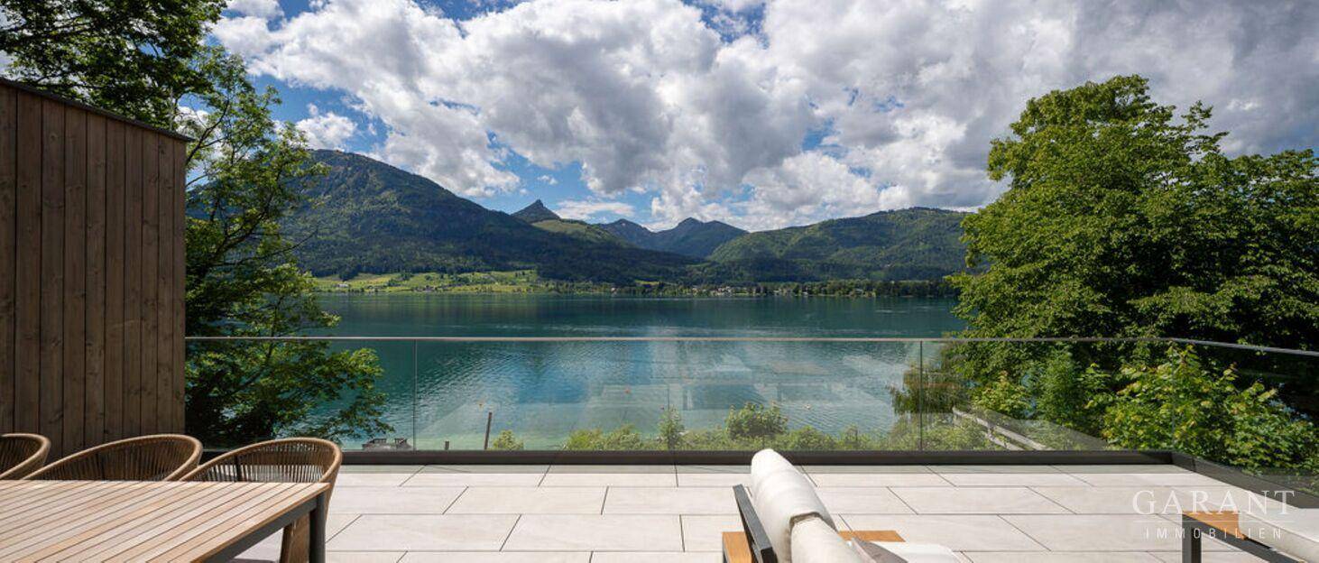 Geräumige Terrasse mit modernen Fliesen, bequemen Liegen und einem atemberaubenden Blick auf den See und die Berge.