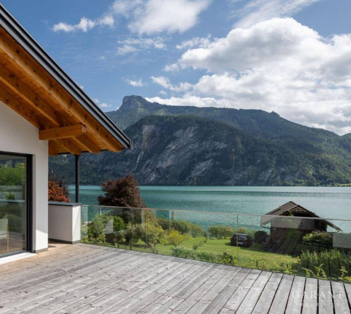 Geräumige Holzterrasse mit Glasgeländer bietet einen atemberaubenden Blick auf den See und die Berge.