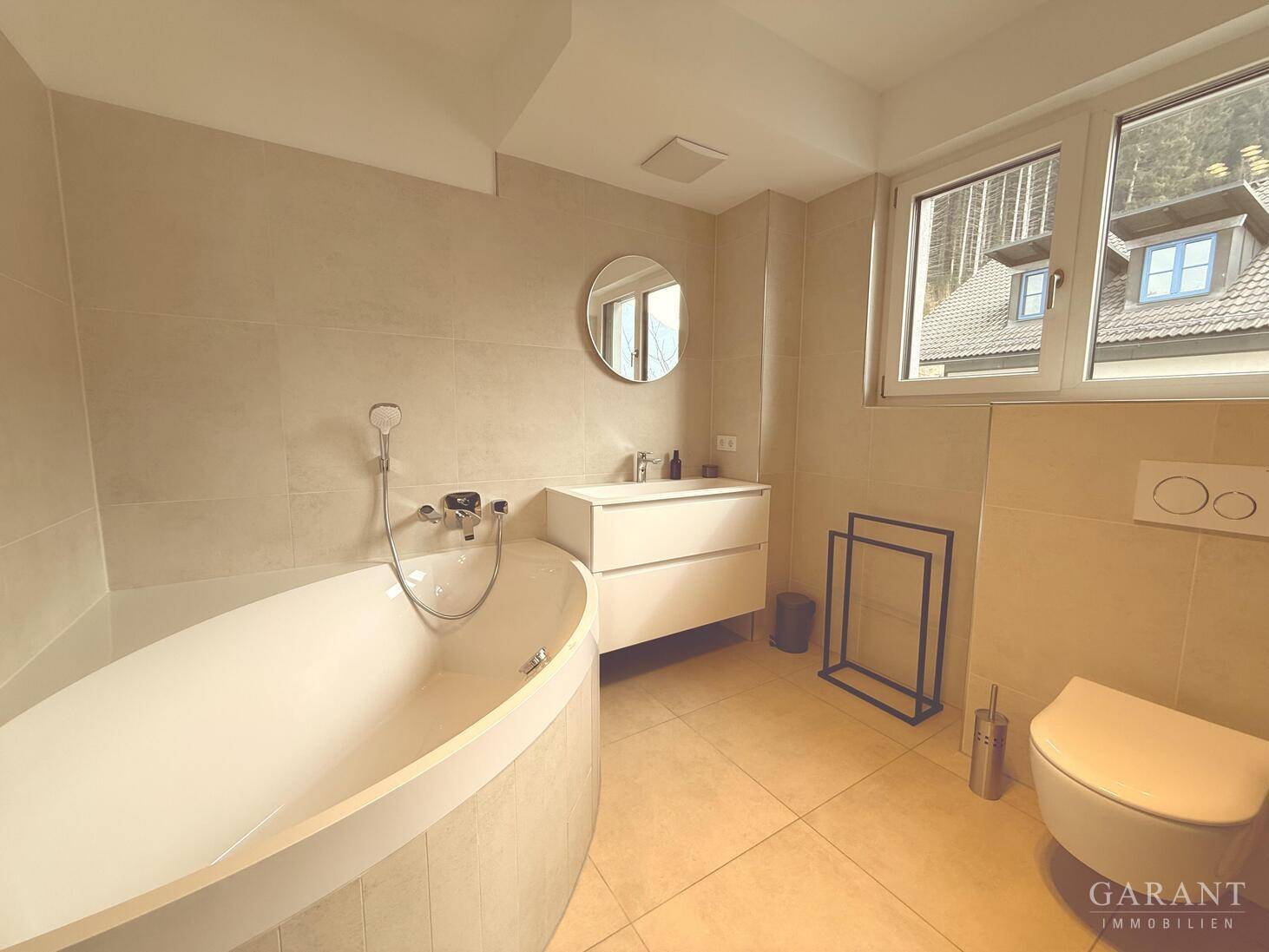 Modernes Badezimmer mit freistehender Badewanne, Wand-WC und Fenster für natürliches Licht.
