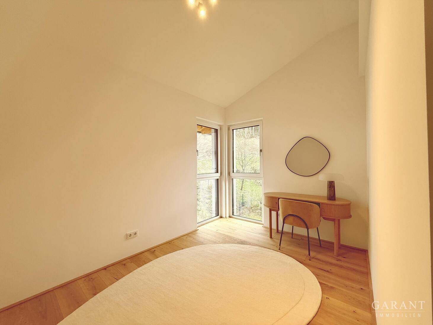 Helles Arbeitszimmer mit Holzboden, schrägen Decken und einem modernen Schreibtisch am Fenster.