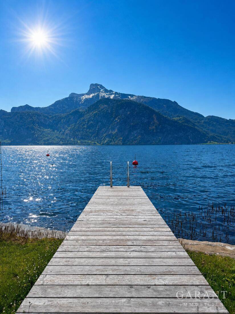 Holzsteg führt in einen klaren Bergsee mit majestätischer Bergkulisse unter strahlendem Sonnenschein.