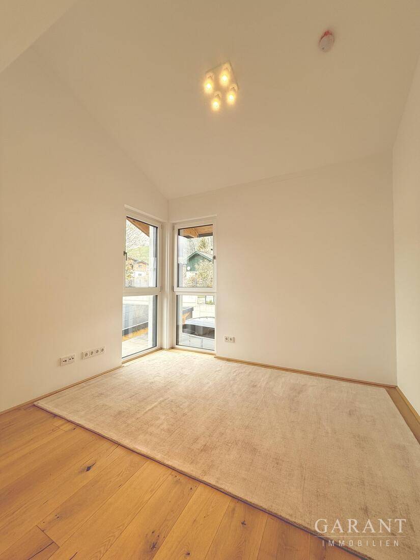 Leeres Zimmer mit Holzboden, weißen Wänden und großen Fenstern, ideal als Schlaf- oder Arbeitszimmer.